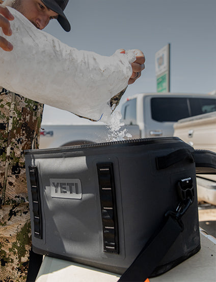 Person pouring ice into a YETI cooler with a truck in the background
