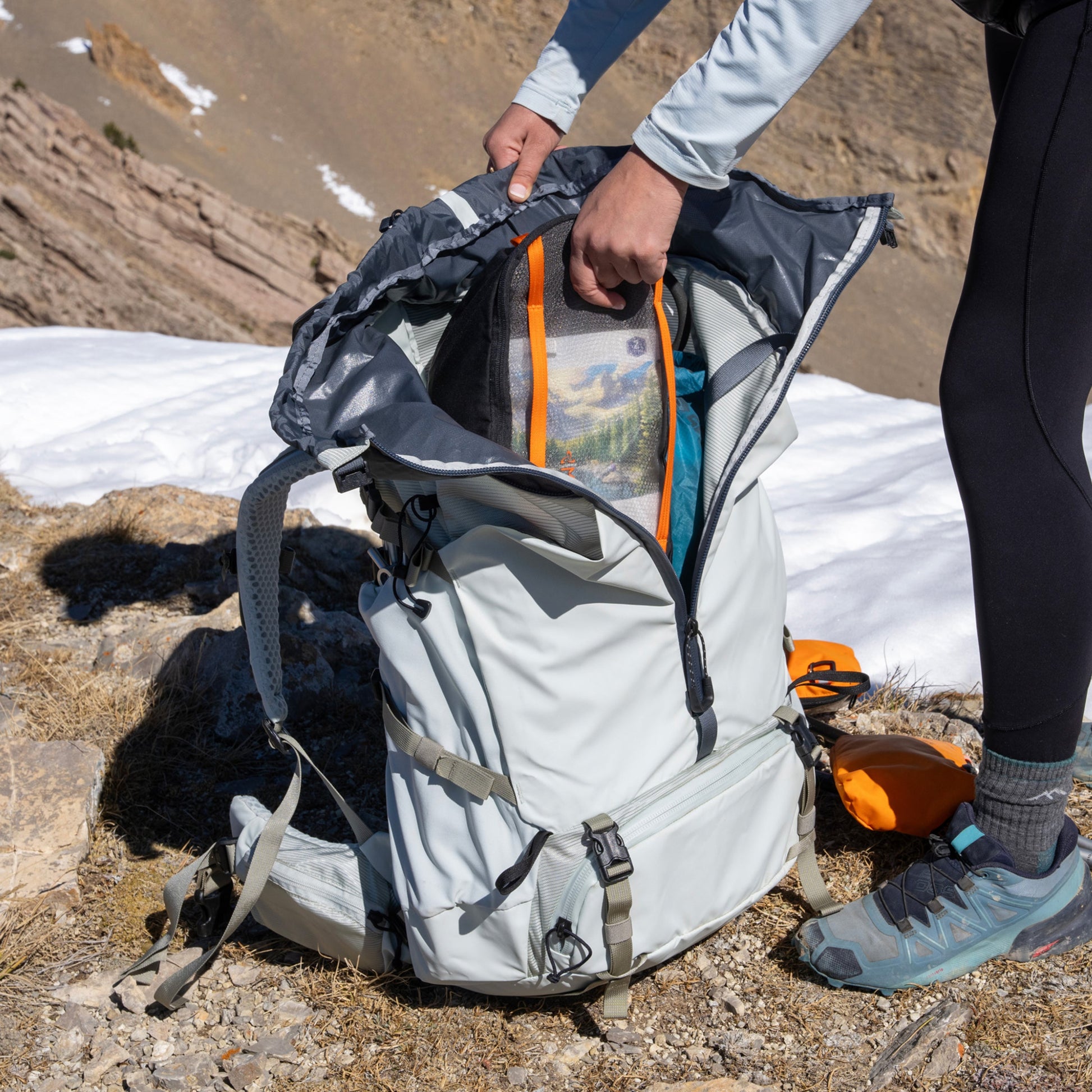 Person opening a backpack in a mountainous area with snow and rocks.