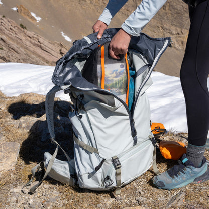 Person opening a backpack in a mountainous area with snow and rocks.