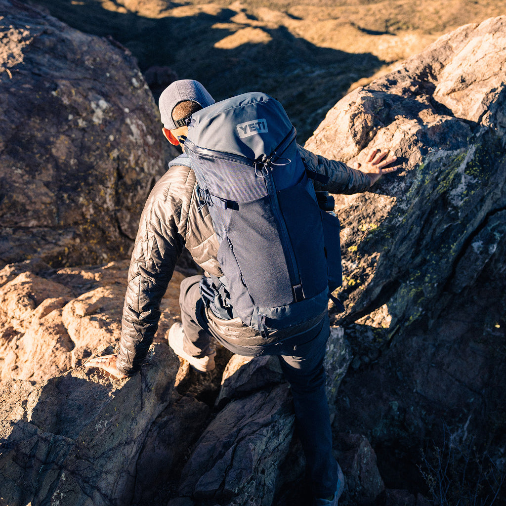 Person climbing a rocky mountain with a YETI backpack.