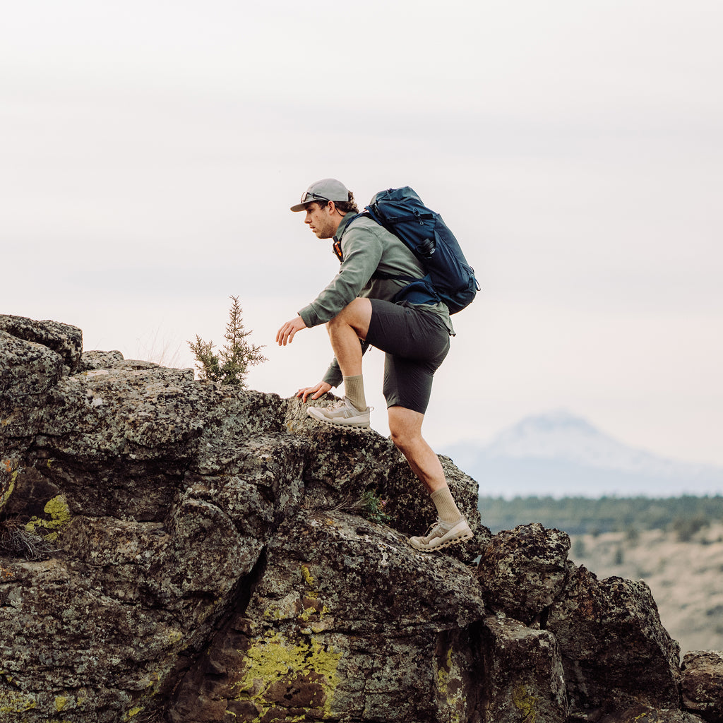 Person with a backpack hiking on rocky terrain with mountains in the background