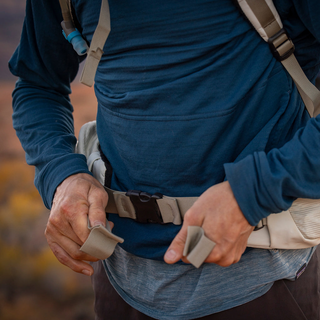 Person adjusting backpack strap against a blurred natural background