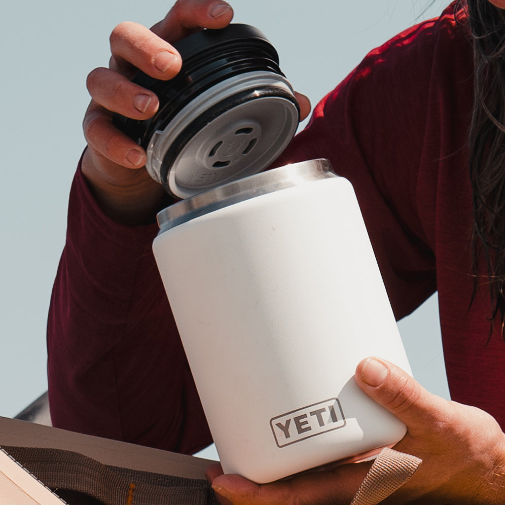 Person holding a YETI food jar with a lid against a clear sky.