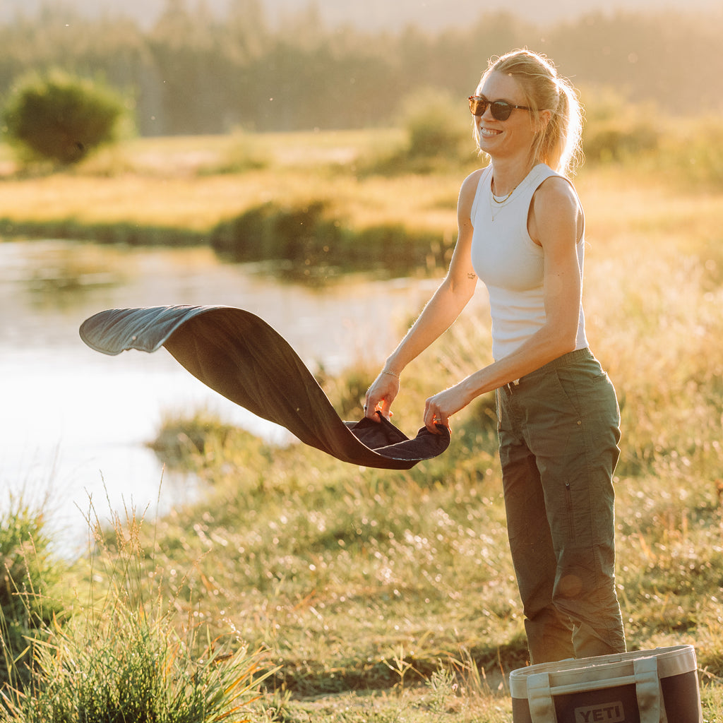 Woman shaking a YETI Small Lowlands Blanket by the river.
