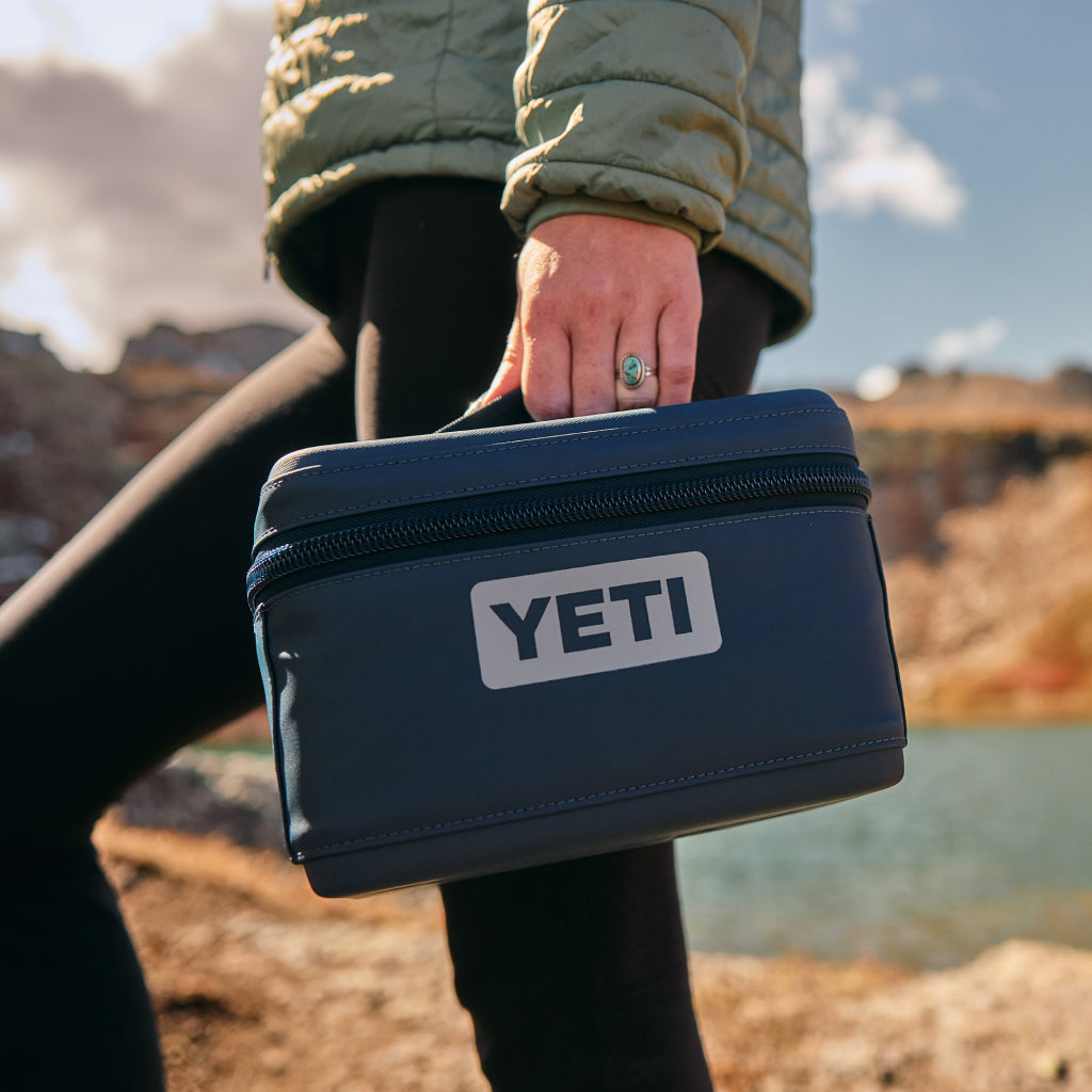Person holding a YETI cooler outdoors with a scenic background