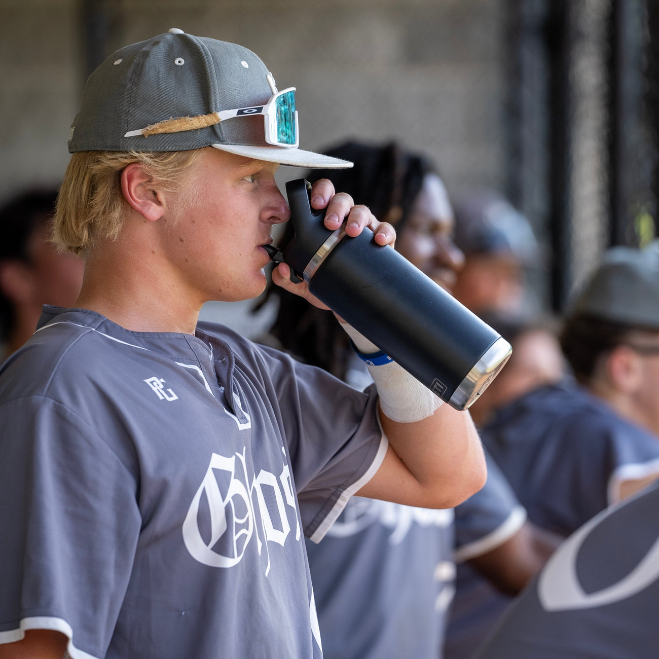 Person in a sports jersey drinking from a YETI black bottle with a straw, surrounded by others in similar attire.