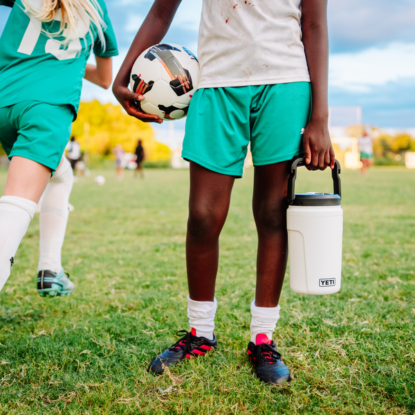 Two people on a football field, one holding a football and the other a Yeti Silo Jug.