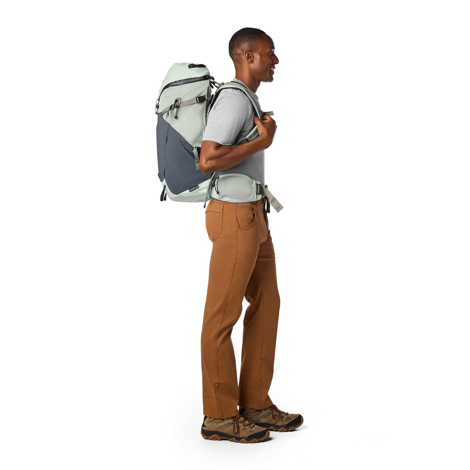 Man wearing a gray backpack and brown pants on a white background